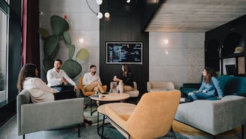 Un espacio lounge moderno con una pantalla grande mostrando un menú, asientos cómodos y una pared decorativa con cactus.