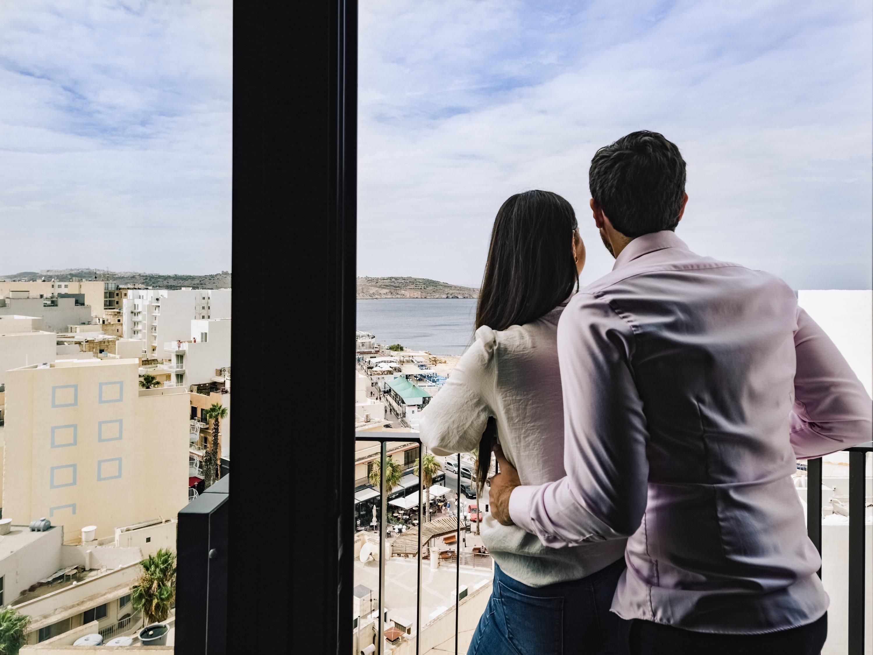 A couple overlooking a coastal cityscape from a balcony.