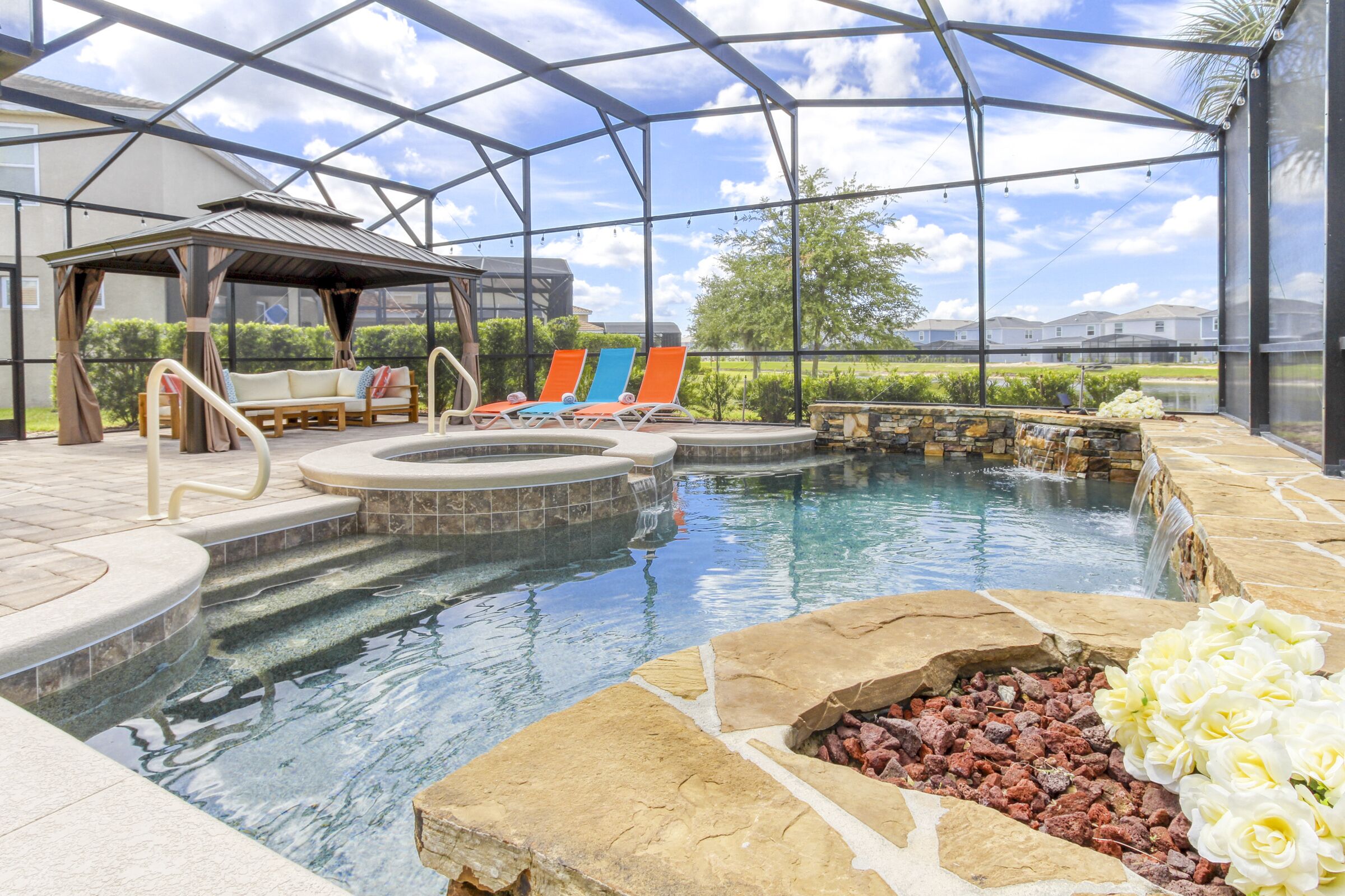 An indoor pool area with lounge chairs, a hot tub, and a stone fire feature.