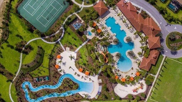 An aerial view of a resort with a large central pool, a tennis court, and a winding water slide. - Marvel Villa - 20 minutes to Disney (Davenport)