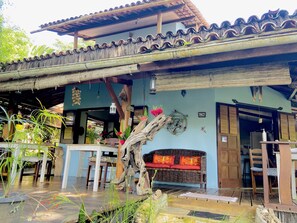 A traditional building with a tiled roof, a wooden porch, and a seating area with a wicker sofa. - Casa Aiti (Cairu)