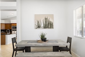 A dining area with a wooden table, four chairs, a potted plant, and a cactus artwork on the wall.
