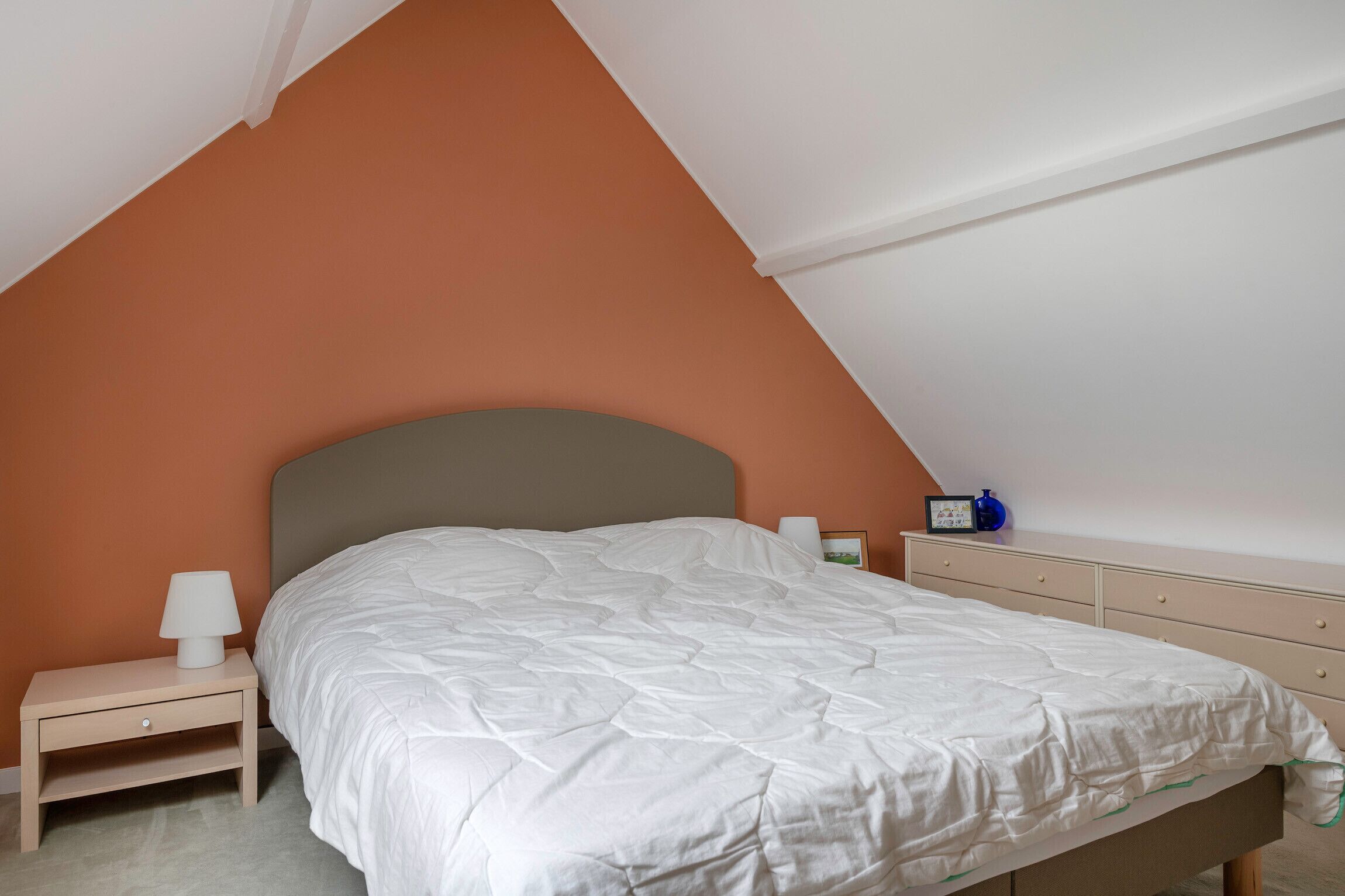 Un dormitorio con cama, mesita de noche, cómoda y lámpara.