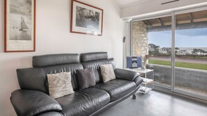 A modern living room with a black leather sofa, two framed pictures on the wall, and a view of the outside through large glass doors. - 300m from the beach, 2 adults - 2 children (Saint-Gildas-de-Rhuys)