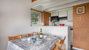 A dining area with a table set for four, a kitchen in the background, and a window with a view of trees. - 300m from the beach, 2 adults - 2 children (Saint-Gildas-de-Rhuys)