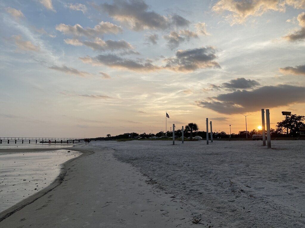 A beach with a pier extending into the water, a clear sky, and a sunset in the background.