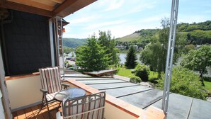 A balcony with a table and chairs, overlooking a river and greenery. - Alone in indoor pool, sauna, steam sauna, directly on the banks of the Moselle, balcony (Zell/Mosel)