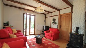 A living room with red sofas, a wooden ceiling, a black stove, and a large window. - Alone in indoor pool, sauna, steam sauna, directly on the banks of the Moselle, balcony (Zell/Mosel)