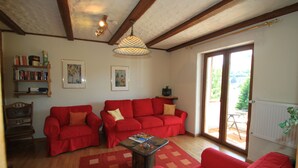 A living room with two red sofas, a wooden coffee table, a bookshelf, and a large window with a view of the outdoors. - Alone in indoor pool, sauna, steam sauna, directly on the banks of the Moselle, balcony (Zell/Mosel)