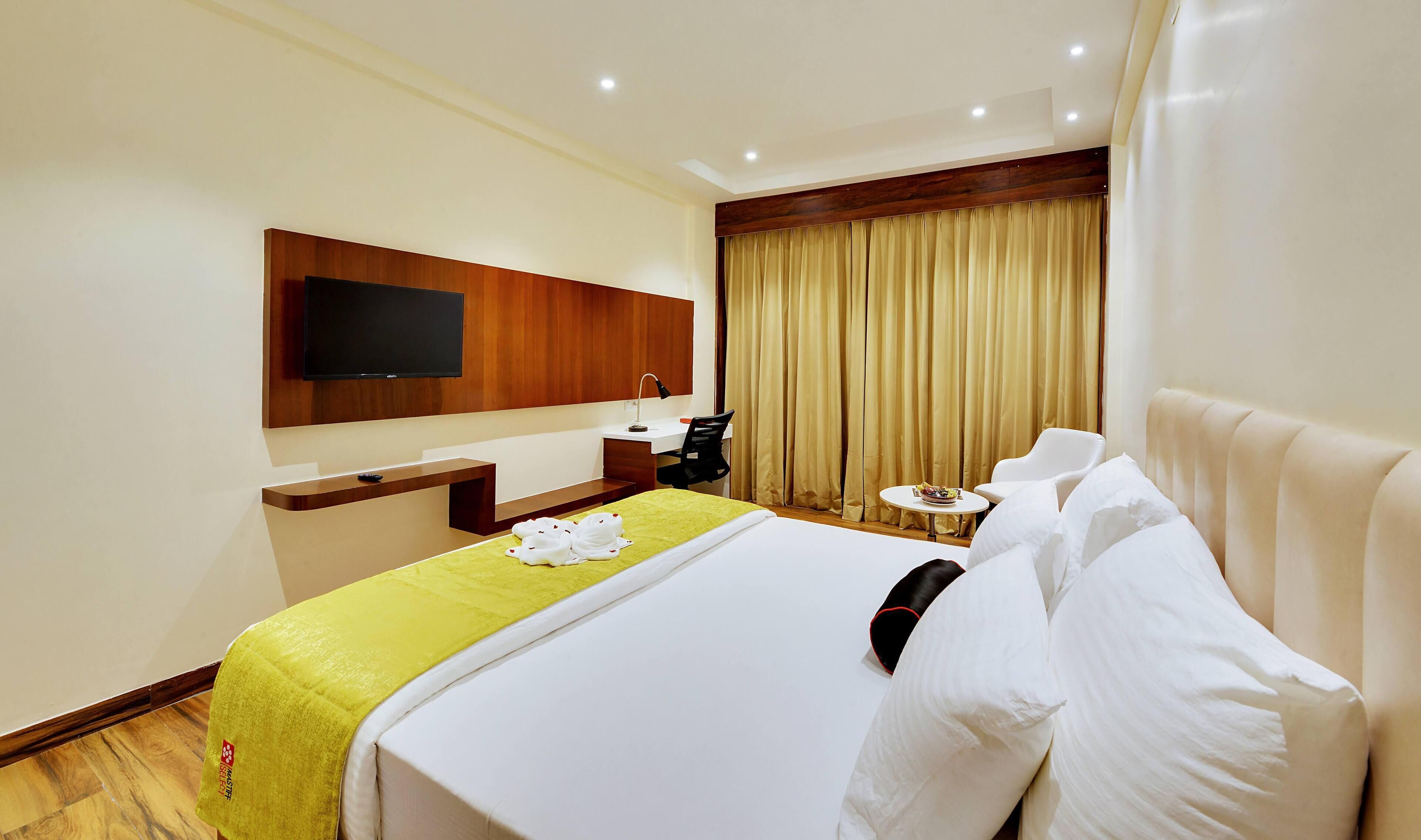 Een hotelkamer met een bed, een bureau, een stoel, een televisie en een raam met gordijnen.