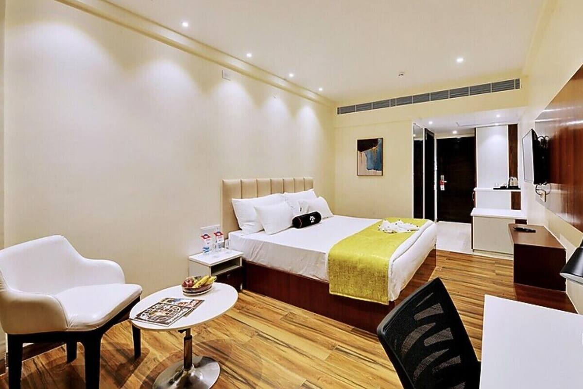 Una habitación de hotel con una cama, un escritorio, una silla, una mesita pequeña y una mesita de noche.