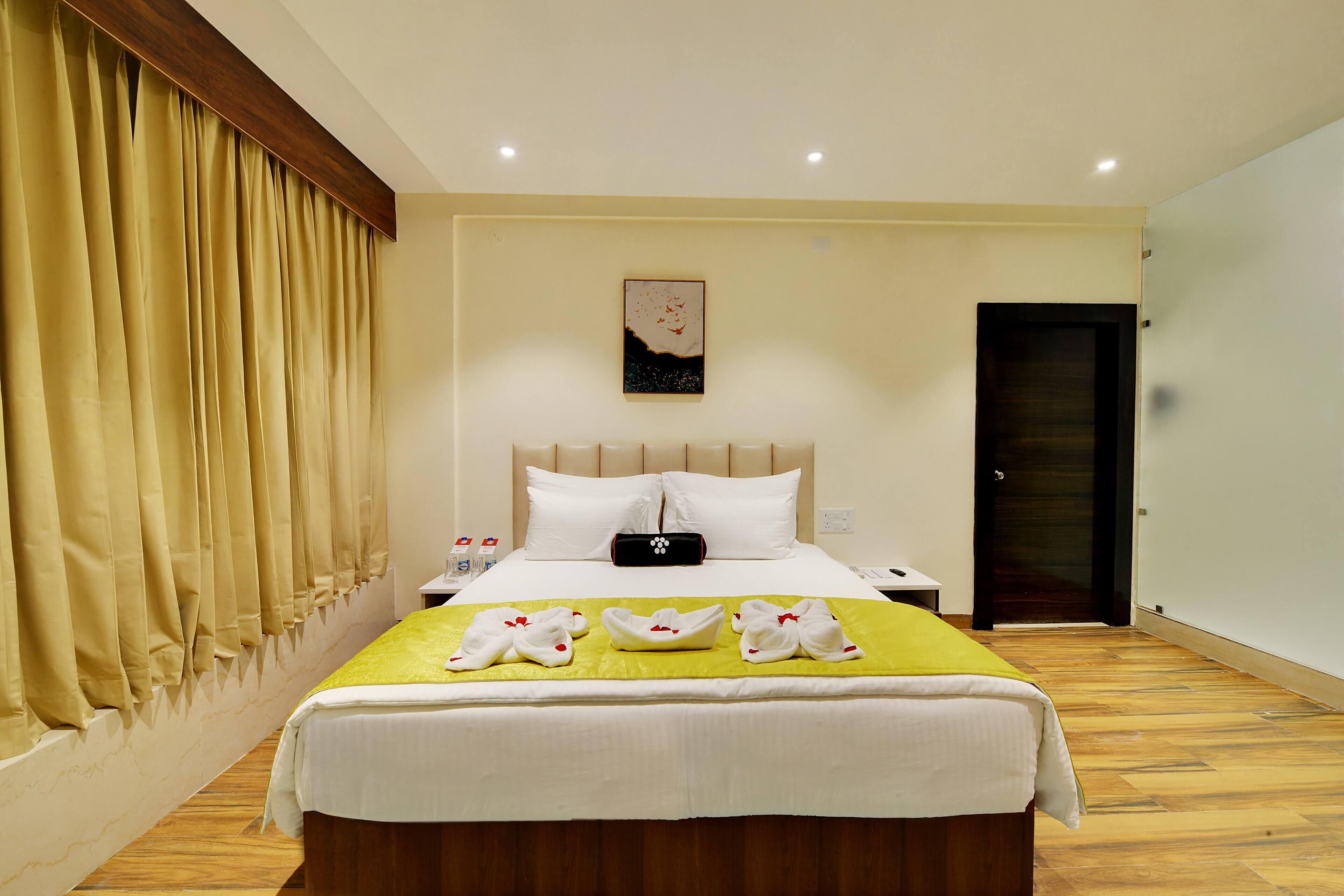 Una habitación de hotel con cama, cortinas, mesita de noche y un cuadro en la pared, además de una puerta.
