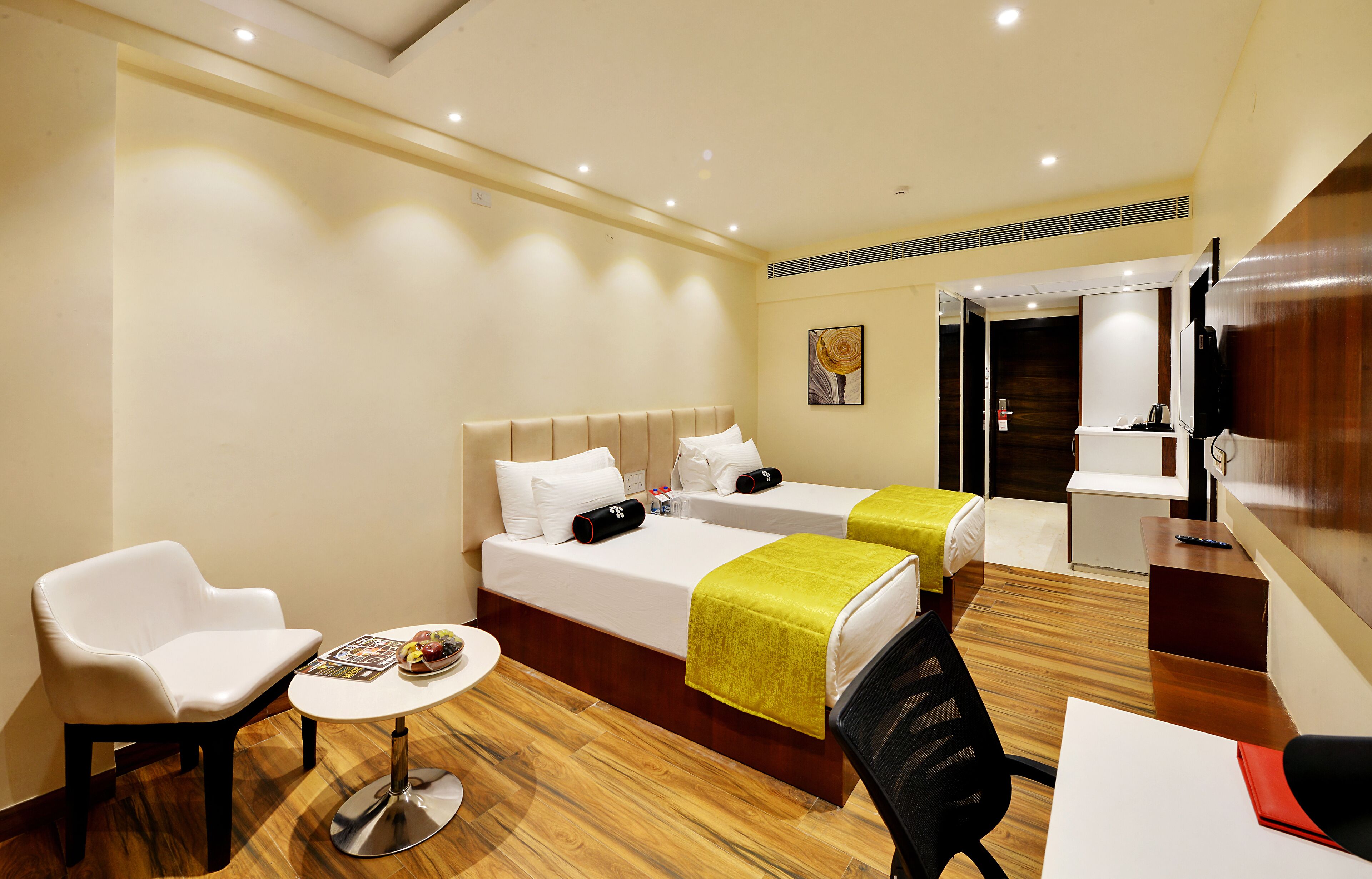 Quarto de hotel com duas camas, uma mesinha com uma cadeira, uma escrivaninha e uma televisão.