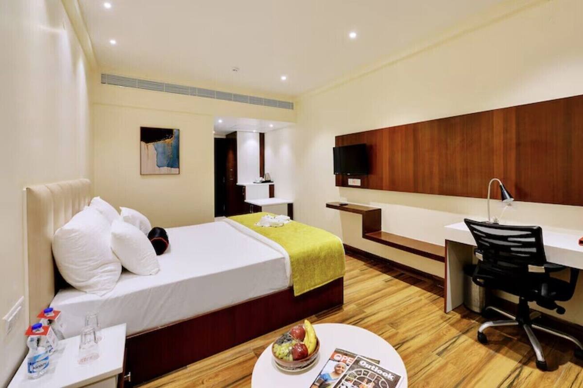 Una habitación de hotel con cama, escritorio, silla, televisor y una mesita con un frutero y una revista.
