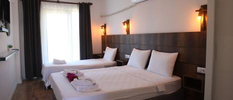 A hotel room with two beds, a wooden headboard, a nightstand, a wall-mounted air conditioner, and a window with curtains.