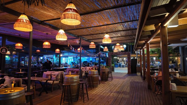 Restaurante al aire libre con mesas de madera, lámparas colgantes y techo de paja.