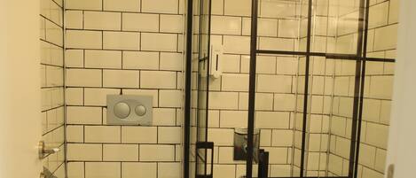 Un baño con ducha acristalada, inodoro y panel de control en la pared.