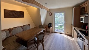 Ein Essbereich mit einem Holztisch und Bänken, eine kleine Küche mit einer Mikrowelle und eine Tür, die auf eine Terrasse im Freien führt.