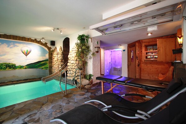 Zona de spa con hidromasaje, camillas de masaje y una pared de piedra con un mural.
