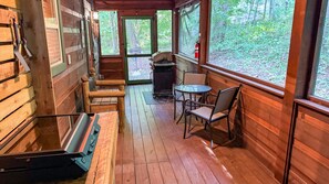 A wooden cabin interior with a porch, a table, chairs, and a grill.