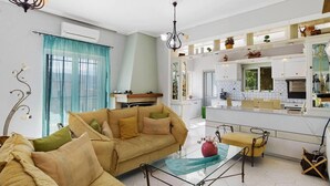 Uma sala de estar moderna com sofá, mesa de centro de vidro e área de cozinha com armários brancos e fogão.