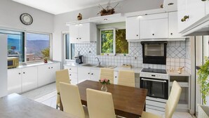 Uma cozinha moderna com armários brancos, uma mesa de jantar com cadeiras, forno embutido e janela com vista para a cidade.