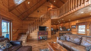 Ein Holzblock-Interieur mit Treppe, Ledersofas, einem Couchtisch und einer Küchenzeile.