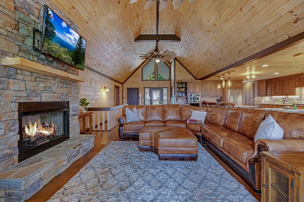 A spacious living room with a stone fireplace, leather sectional sofa, and a large TV mounted on the wall. - Happy Hour Heights Blue Ridge, GA (Blue Ridge)