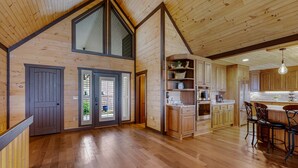 A spacious kitchen with wooden cabinetry, a central island with bar stools, and a large window above the sink. - Happy Hour Heights – Blue Ridge, Ga. (Blue Ridge)
