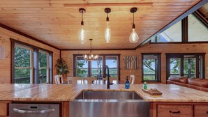 A kitchen with wooden cabinets, a stainless steel sink, and a dining area with a table and chairs. - Happy Hour Heights – Blue Ridge, Ga. (Blue Ridge)