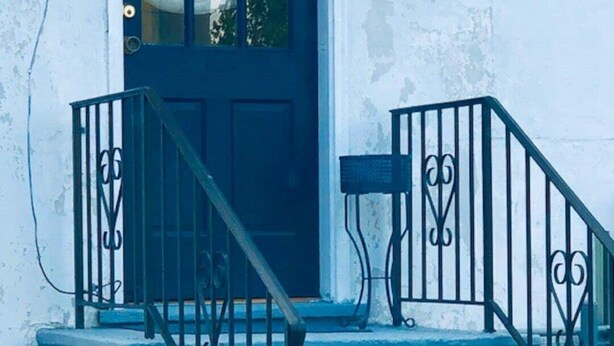 A white building with a black door and a set of blue-painted stairs with black railings.