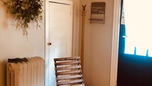 A room with a radiator, a wooden rocking chair, a door, and a window with a lace curtain.