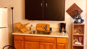 A compact kitchen with wooden cabinets, a sink, a coffee maker, and a shelf with kitchenware.