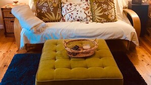 A cozy bedroom with a bed, two pillows, a green ottoman, a painting on the wall, and two bedside lamps.