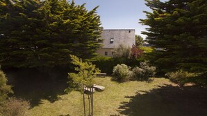 A building surrounded by dense evergreen trees and a grassy area with a bench. - Self-contained apartment in Breton house (Loctudy)
