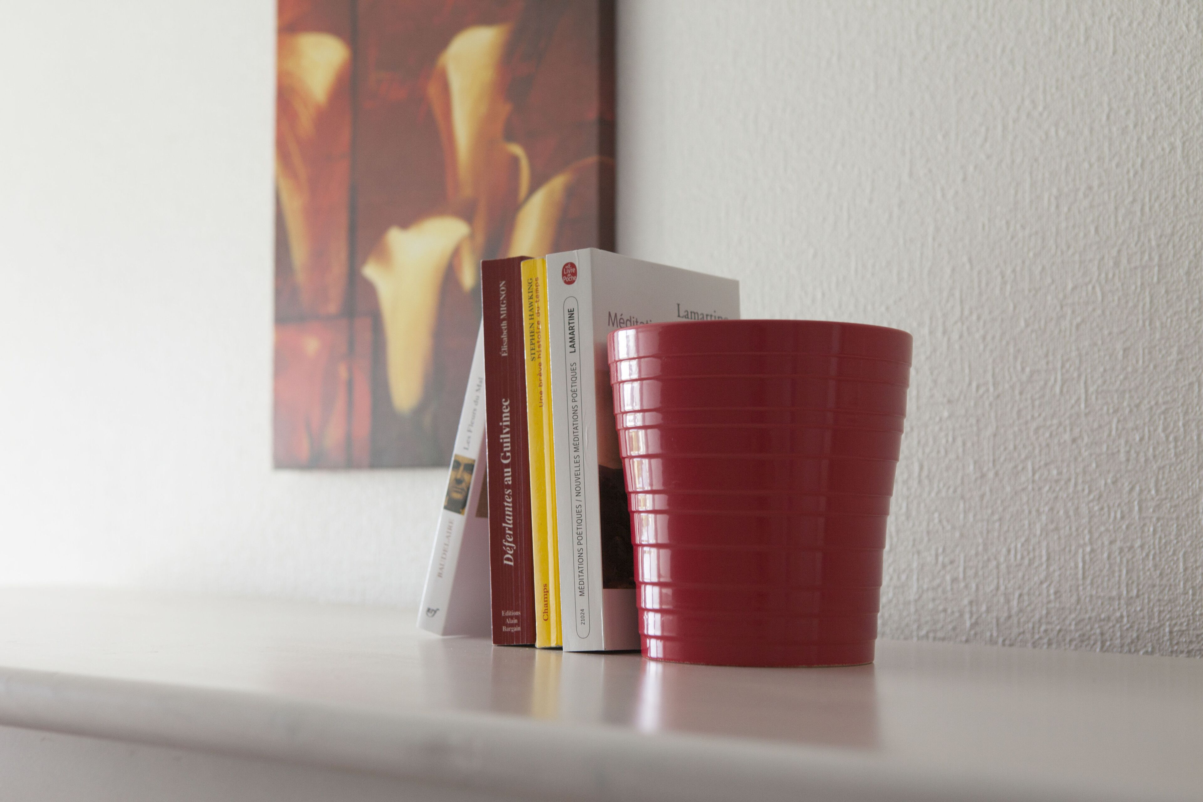 A stack of books on a white surface with a red cup beside them.