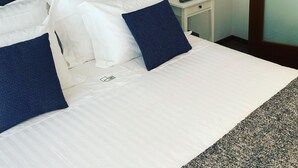 A neatly made bed with white and navy blue bedding, a bedside table with a lamp and a small plant, and two framed pictures on the wall. - Oporto City Center Apartment with terrace (Porto)
