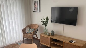 A living room with a wicker chair, a sofa, a TV on the wall, and a wooden console table. - Oporto City Center Apartment with terrace (Porto)