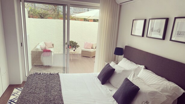 A bedroom with a bed, a large window, and a view of an outdoor seating area. - Oporto City Center Apartment with terrace (Porto)