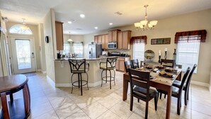A spacious kitchen with a central island, bar stools, and a dining area with a table and chairs. - Palace Retreat - Private Pool/Spa & 24/7 Support (Davenport)