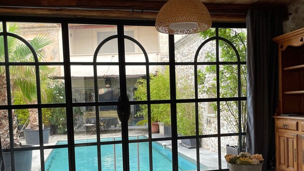 Une pièce dotée d’une grande fenêtre donnant sur une piscine, d’un plafond en bois et d’un coin salon agrémenté de coussins.