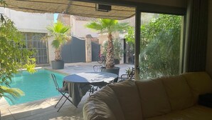 Une terrasse ensoleillée avec une piscine, un canapé en cuir et des plantes en pot.