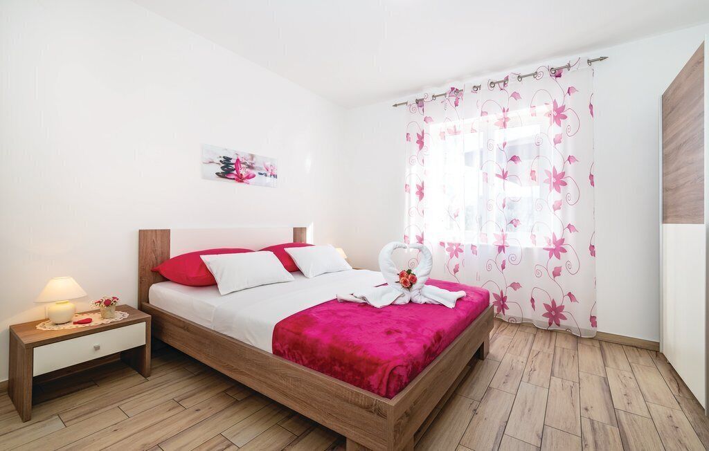 Un letto rifatto con una coperta rossa e cuscini bianchi, un comodino con una lampada e una tenda con motivo floreale.