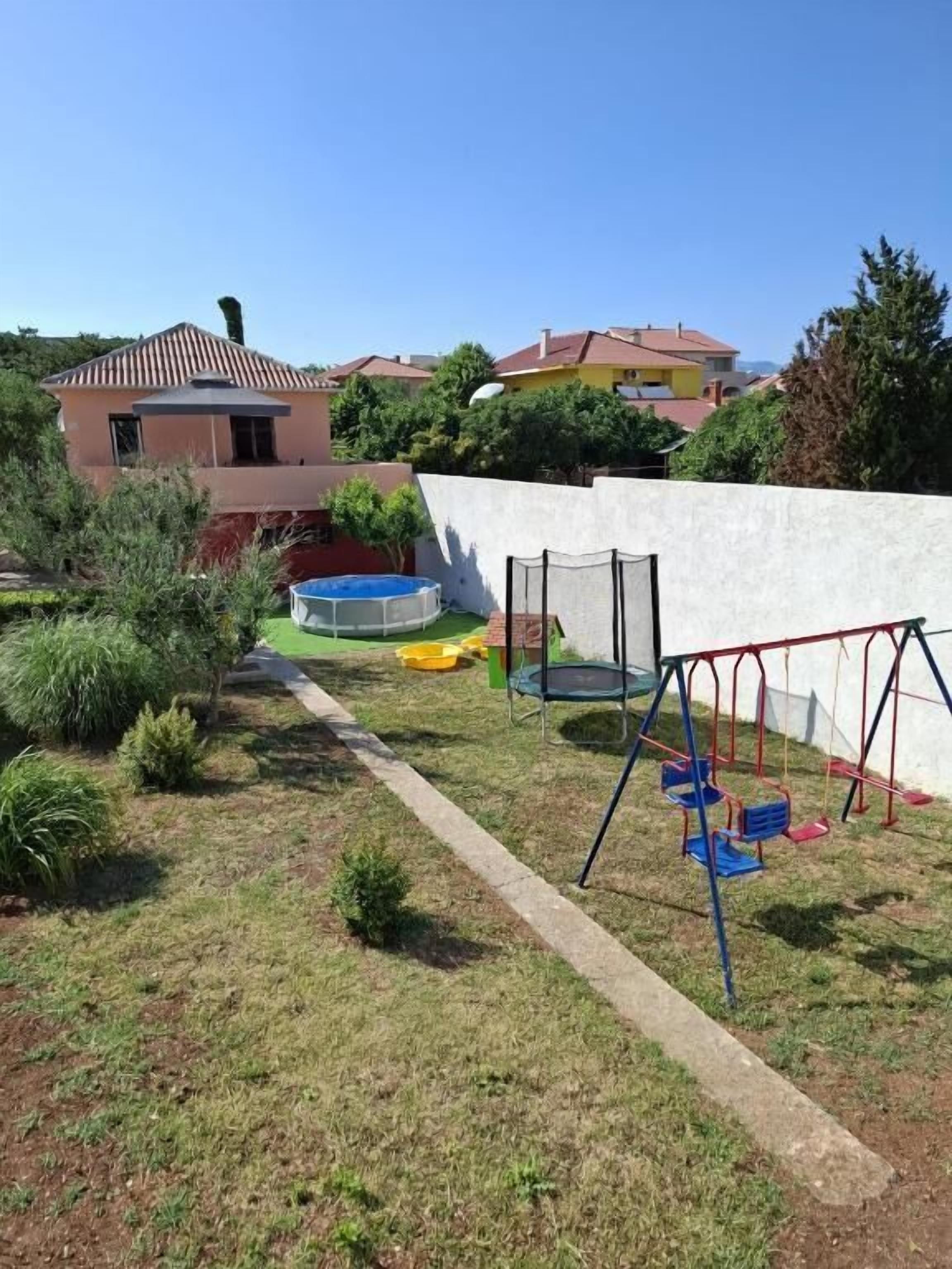 Un patio trasero con un trampolín, un conjunto de columpios y una piscina pequeña.