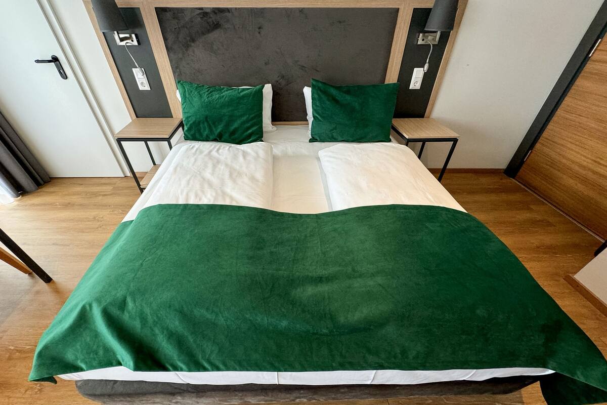 Un lit bien fait, recouvert d’une couvre-lit verte et blanche, avec deux oreillers verts et une tête de lit en bois.