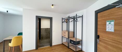 Een kamer met een houten vloer, een bureau met stoel, een kledingkast met hanggedeelte en een deur met een bordje.
