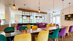 A modern restaurant with colorful seating, wooden tables, and pendant lighting. - DORMERO Hotel Rüsselsheim (Ruesselsheim)