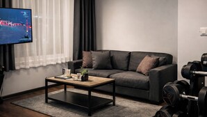 A modern living room with a grey sofa, a coffee table, a TV on a stand, and a set of dumbbells. - DORMERO Hotel Rüsselsheim (Ruesselsheim)