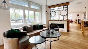 A modern living room with a sofa, two round tables, and a fireplace. - DORMERO Hotel Rüsselsheim (Ruesselsheim)