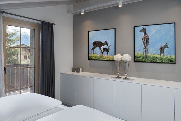 A hotel room with a large window, a bed, a white cabinet, and two framed pictures of deer on the wall.